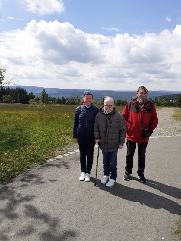 Tatsiana Litzinger, Martin Jonas und Klaus Becker stehen auf einem Weg. Hinter ihnen ist eine weite, grüne Landschaft und blauer Himmel mit weißen Wolken.