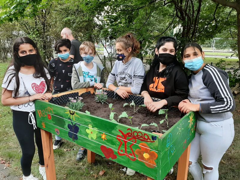 Erfolgreich eingesetzt - sechs Kinder aus Klasse 8a der Werner-von-Siemens-Schule stehen rund um ihr bunt bemaltes und bepflanztes Hochbeet im Garten des Wichern-Hauses.