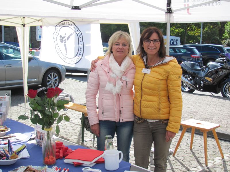 Zwei Frauen stehen hinter einem Tisch und lächeln in die Kamera