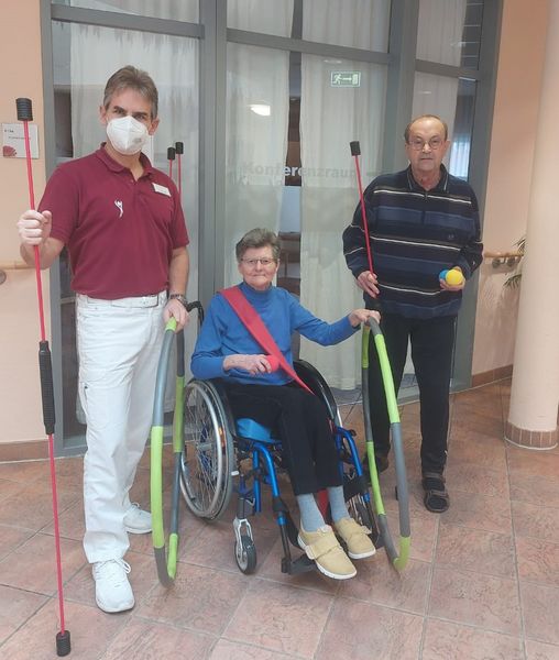 Ein Physiotherapeut mit zwei Bewohnern, die Schwingstäbe und Hula-Hoop-Reifen in den Händen halten