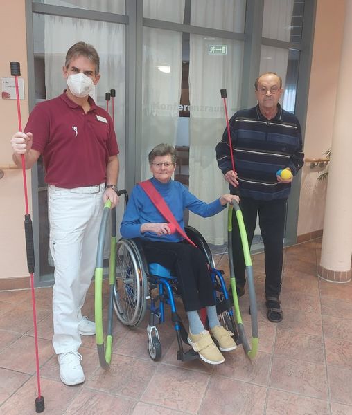 Neue Trainingsgeräte für das Albert-Schweitzer-Haus Ein Physiotherapeut mit zwei Bewohnern, die Schwingstäbe und Hula-Hoop-Reifen in den Händen halten