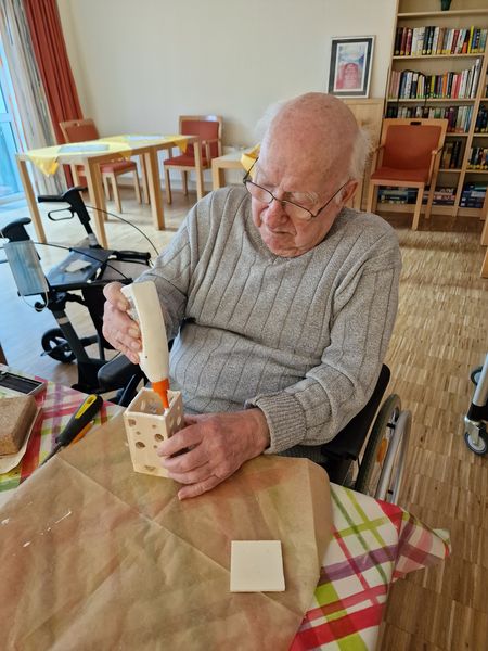 Teelichthalter aus Holz herstellen Ein Mann im Rollsuhl sitzt an einem Tisch und ist dabei, Holz zusammenzuleimen.