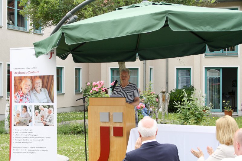 Hausleiterin Manuela Schock steht draußen an einem Rednerpult unter einem Sonnenschirm. Daneben steht ein Banner mit dem neuen Namen Stephanus-Zentrum.