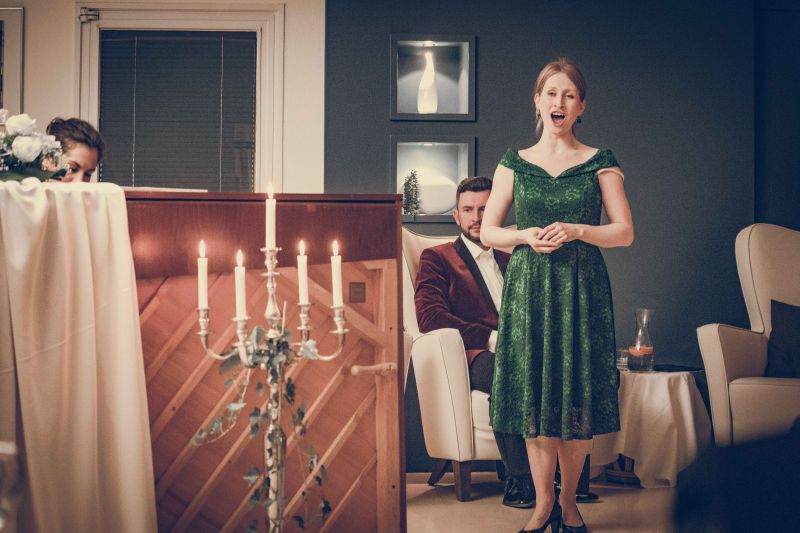 Frau steht neben einem Klavier in grünem Kleid und singt