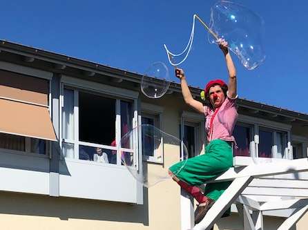 Bewohnerinnen des Albert-Schweitzer-Hauses freuen sich am offenen Fenster über die Riesenseifenblasen von Clownsfrau Ilse, die im Garten der Einrichtung für Abwechslung sorgt.