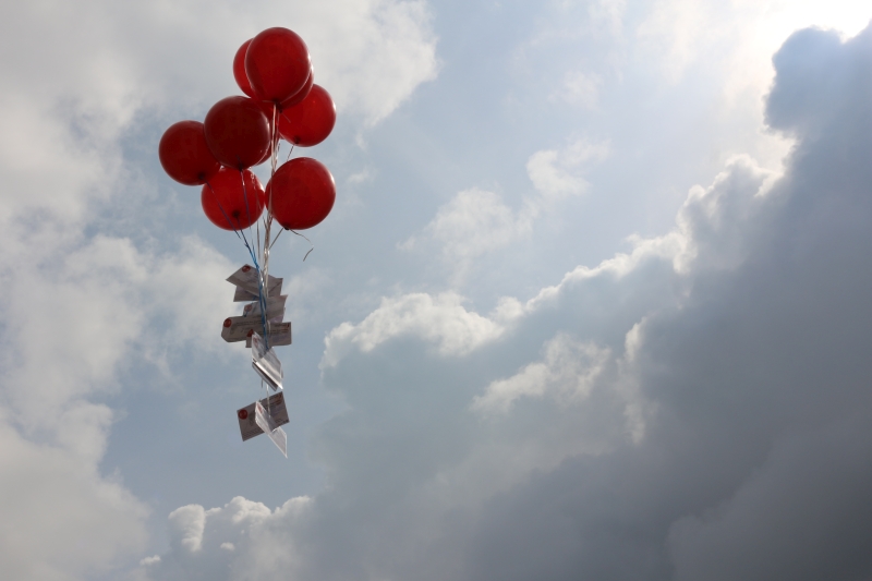 Wunschkarten gegen die Einsamkeit gehen auf die Reise... ein großes Bündel roter Luftballons mit Wünsche für besondere Augenblicke schwebt in Beckum am Himmel