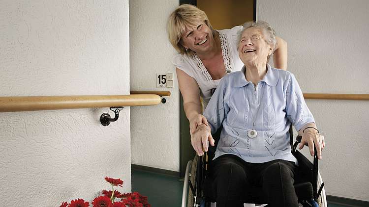 Eine Frau schiebt eine ältere Dame im Rollstuhl