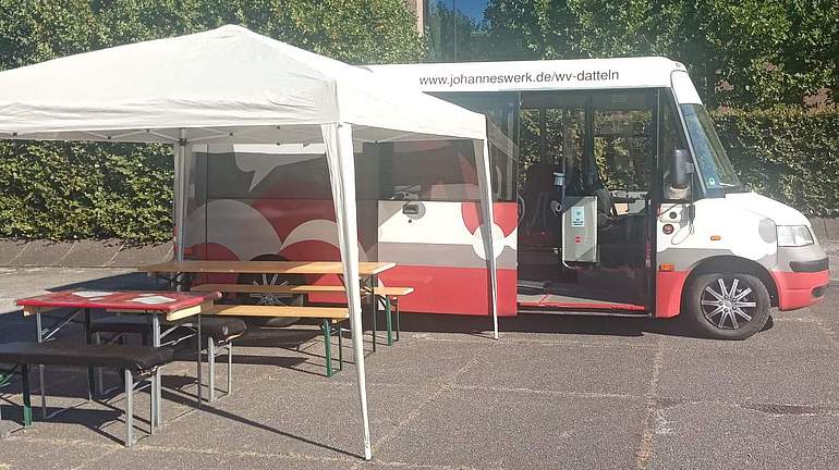 Vor dem Jo-Mobil-Bus ist ein Pavillon aufgebaut, unter dem Tische und Bänke stehen