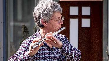 Eine Frau mit grauen Haaren und Brille, die Querflöte spielt
