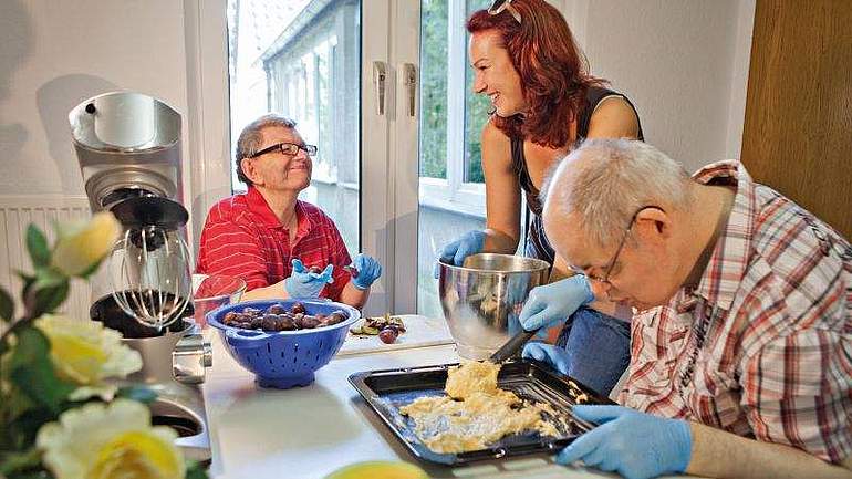 Zwei Männder und eine Frau backen einen Kuchen