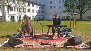 Musiker mit Cello und Keyboard auf einem Teppich im Garten