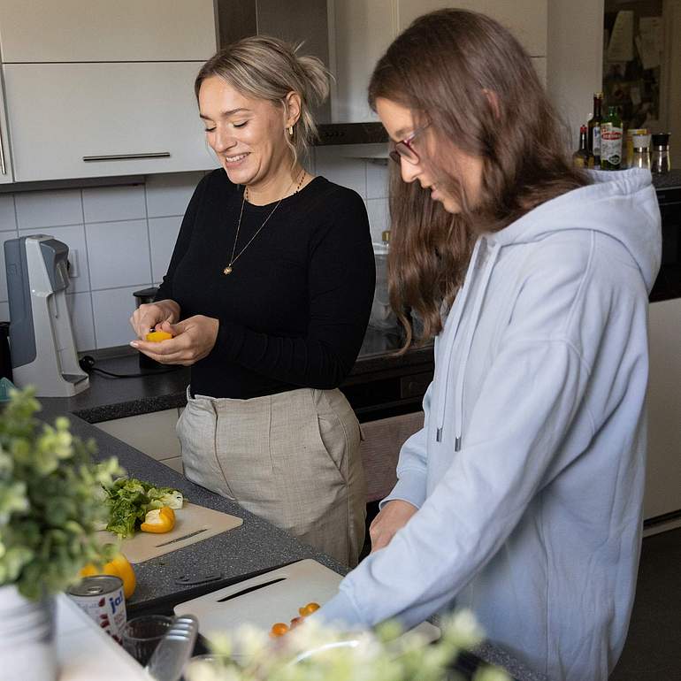 Zwei Frauen stehen in einer Küche und schneiden Gemüse. 