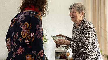 Gisela Schulte hält ein Foto in beiden Händen, dass sie einer Mitarbeiterin des Altenheims zeigt.