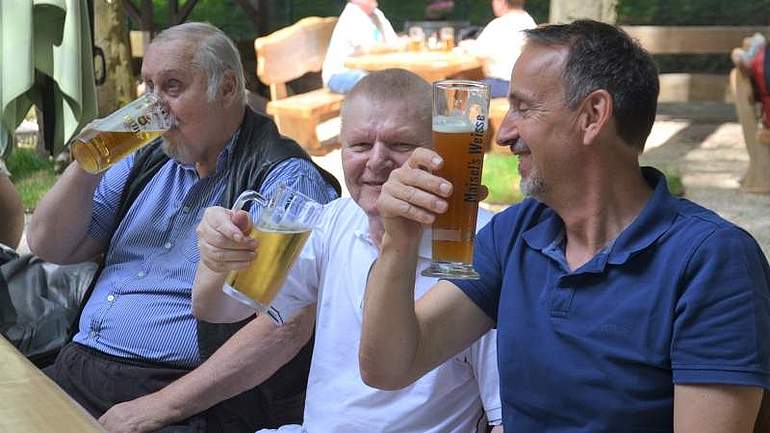 Drei Männer genießen ihr Bier bei Sonnenschein im Biergarten