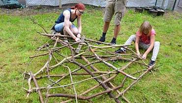 Bei LandArt wird mit Naturmaterialien gebaut und gebastelt Zwei Mädchen, die aus Ästen ein Gerüst bauen
