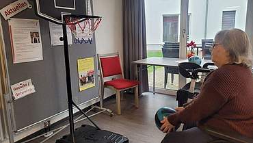 Der neue Basketballkorb wird von den Bewohner*innen direkt ausprobiert. Eine Bewohnerin sitzt vor einem Basketballkorb und hat einen Ball in der Hand