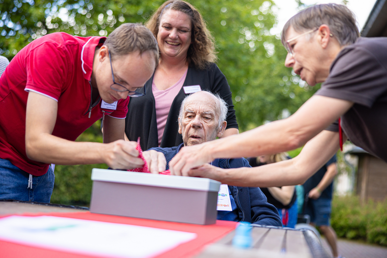 Zwei Betreuungskräfte helfen einem Bewohner, seine Hand in einen Fühlkasten zu stecken 