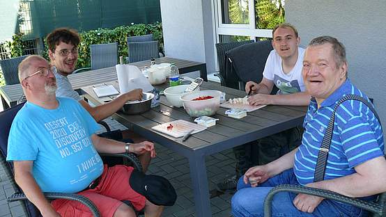 Vier Männer, die an einem Gartentisch sitzen und einen Salat vorbereiten