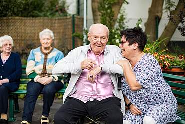 Alter Herr und Frau mit kurzen schwarzen Haaren sitzen auf einer Bank und lachen sich an