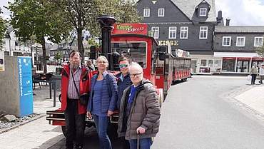Vier Personen stehen vor einer roten Bimmelbahn in Winterberg