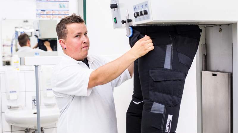 Ein Mann mit weißem T-Shirt bügelt eine Hose