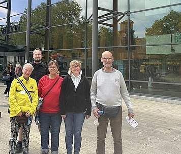 Fünf Menschen stehen nebeneinander vor einem Gebäude aus Glas