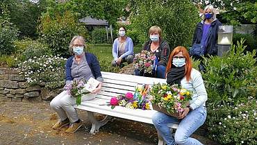 Fünf Frauen mit Masken und Wildblumensträußen