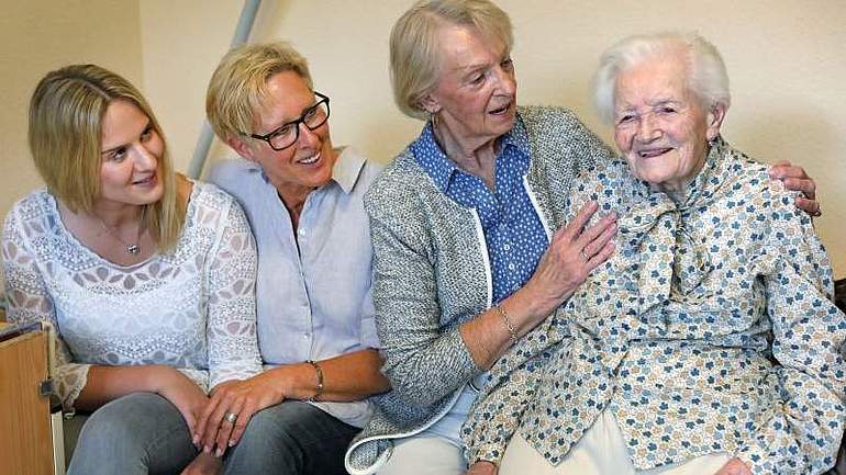Vier Frauen verschiedenen Alters sitzen nebeneinander auf einem Pflegebett