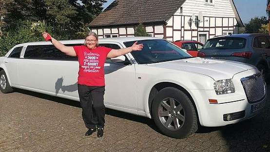 Eine Frau mit roten T-Shirt steht vor einer weißen Limousine